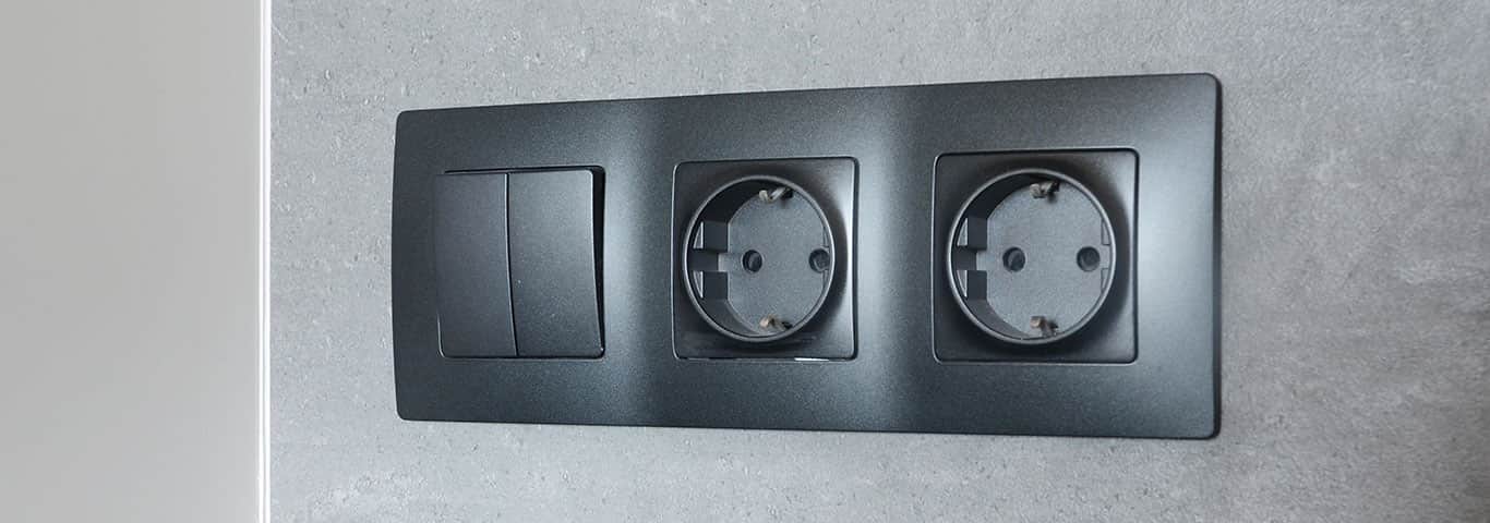 Nowoczesne czarne gniazdko elektryczne zamontowane na szarej ścianie w kuchni