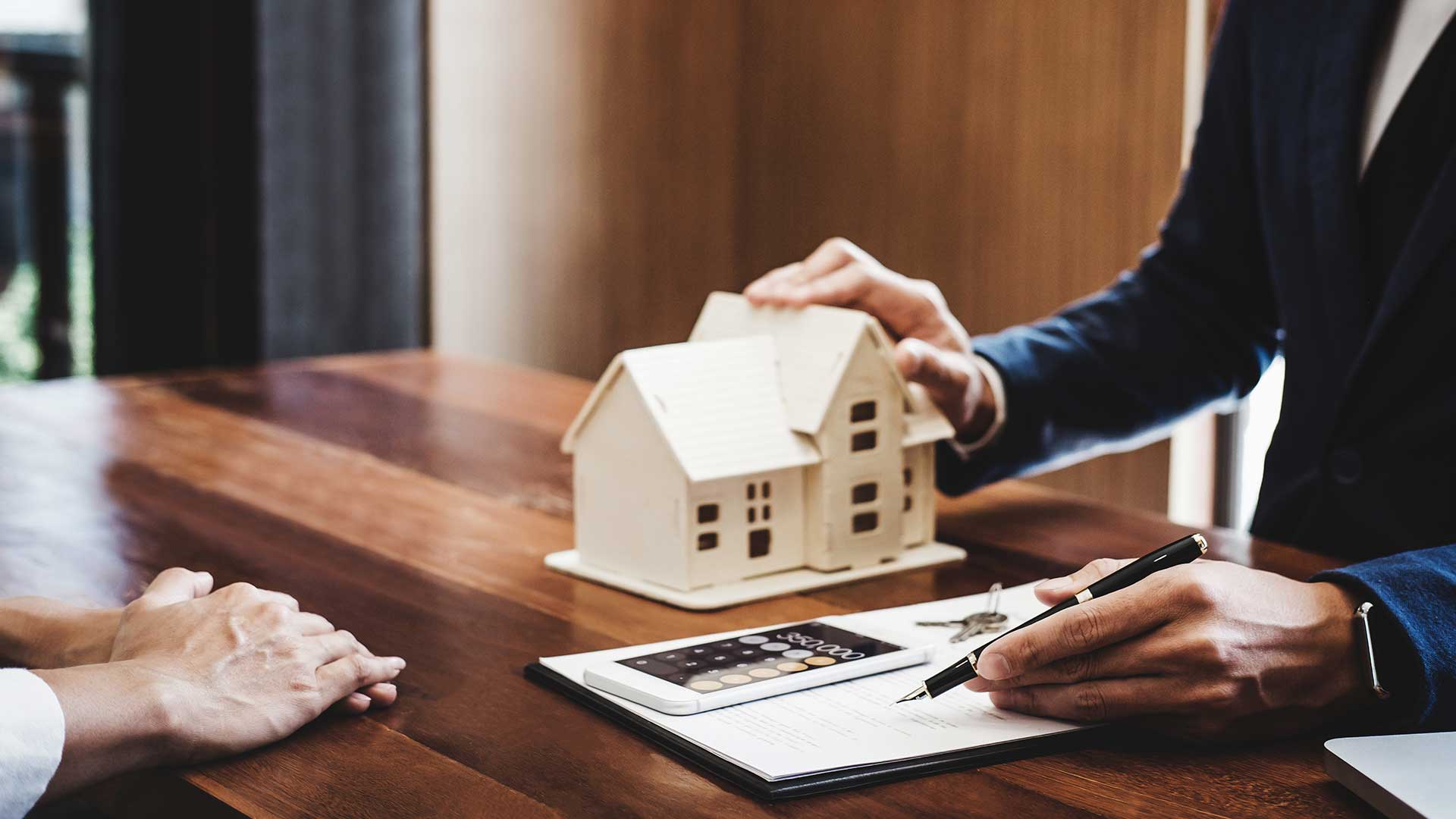 doradca kredytowy wyjaśnia klientowi warunki kredytu hipotecznego trzymając w jednej ręce długopis a w drugiej mały domek -  w 2023