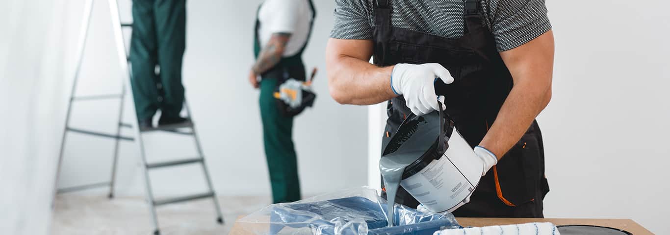 Fachowiec przygotowuje farbę do malowania, a w tle ekipa remontowa pracuje przy ścianach