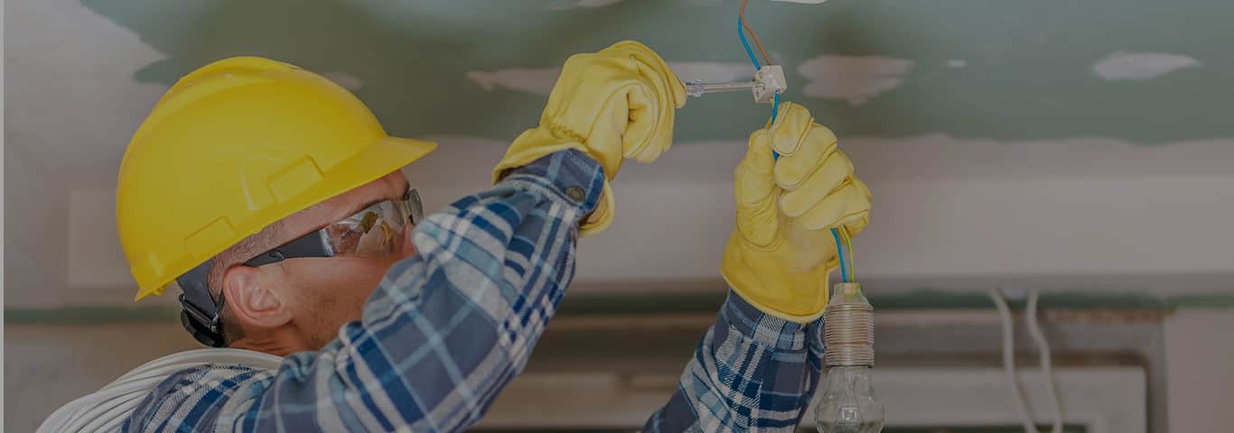 Specjalista elektryk w kasku ochronnym montuje przewody elektryczne podczas instalacji w domu