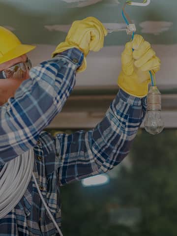 Specjalista elektryk w kasku ochronnym montuje przewody elektryczne podczas instalacji w domu
