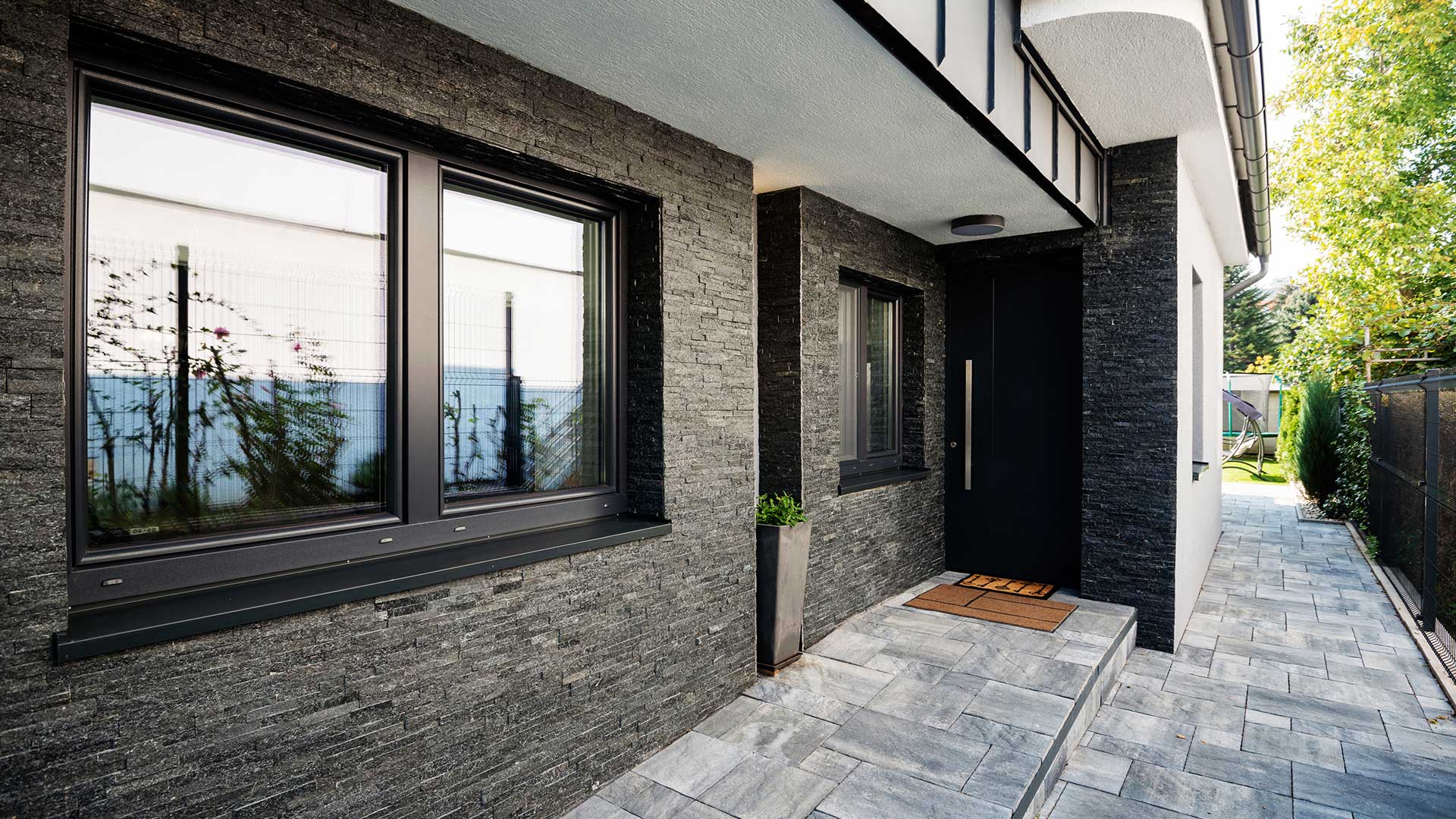 front domu z nowoczesną elewacją z kamienia i oknami z czarnymi framugami