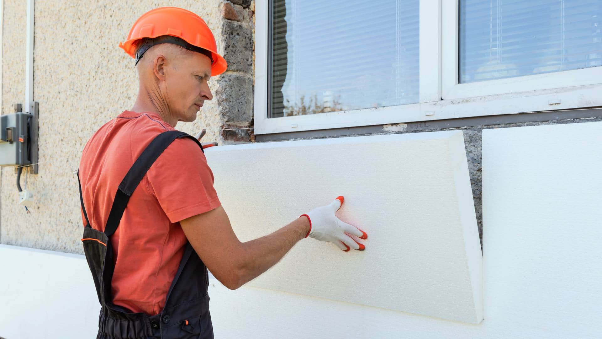 Fachowiec montujący płyty styropianowe na ścianie zewnętrznej domu podczas ocieplania budynku