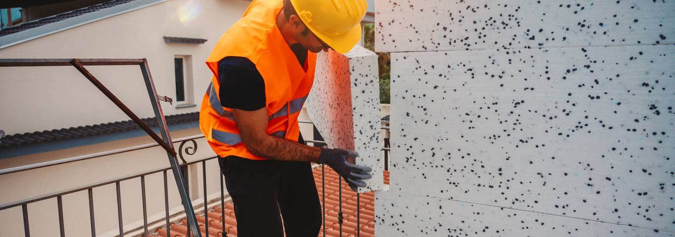 Fachowiec z kaskiem i rękawicami montuje styropian na zewnętrznej ścianie domu – przykład profesjonalnego wykonania elewacji
