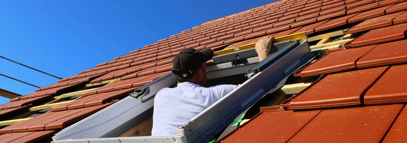 fachowiec montuje okno dachowe na czerwonym dachu