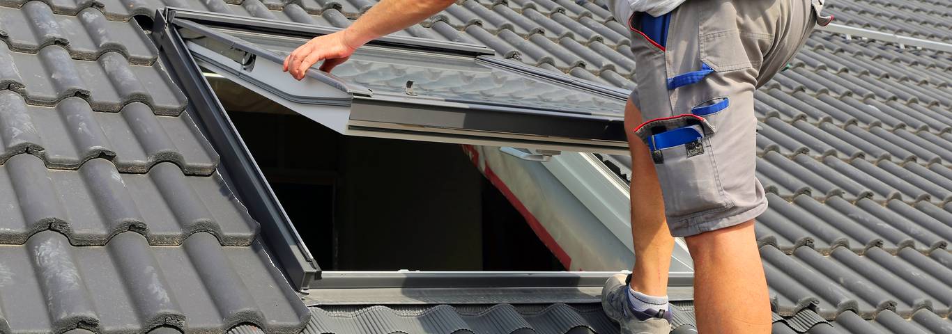 fachowiec montuje okno dachowe stojac na dachu