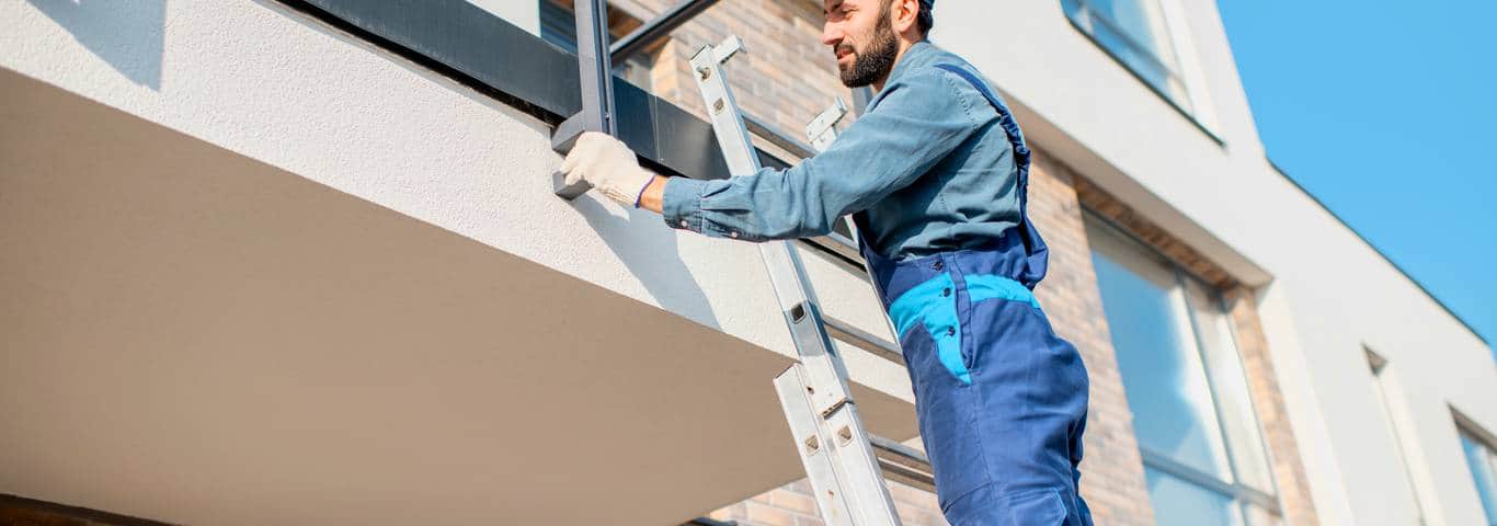 fachowiec w stroju budowlanym stoi na drabinie i sprawdza wykonanie ocieplenia balkonu styropianem