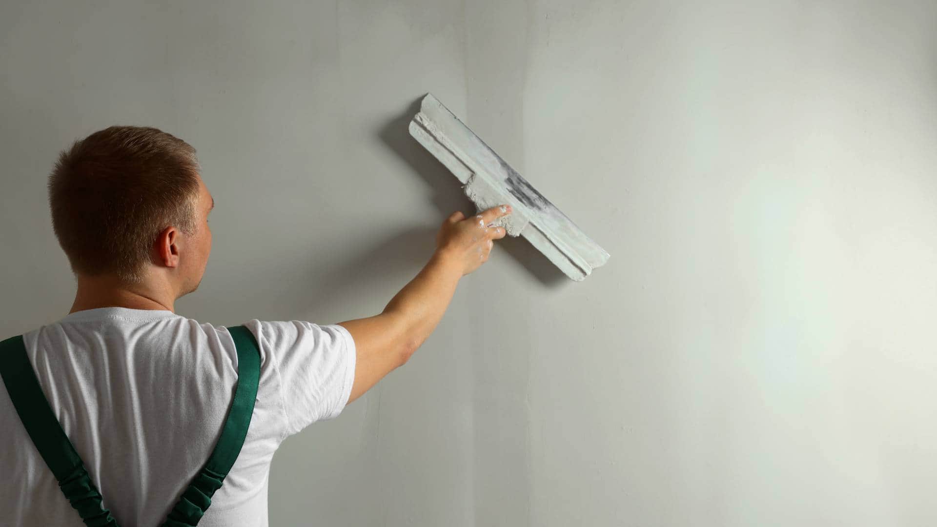 Fachowiec nakłada gładź na ścianę szeroką szpachlą podczas wykończenia wnętrza