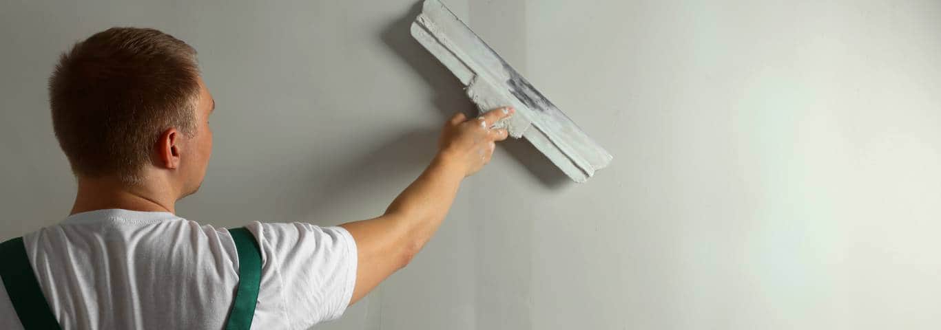 Fachowiec nakłada gładź na ścianę szeroką szpachlą podczas wykończenia wnętrza