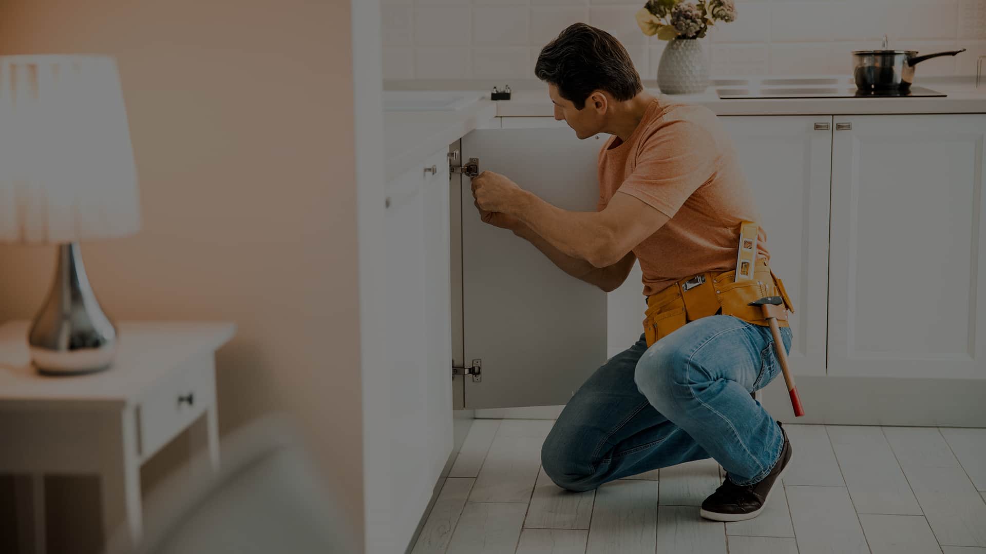 Fachowiec naprawiający szafkę kuchenną, w tle widoczna płyta grzewcza z garnkiem