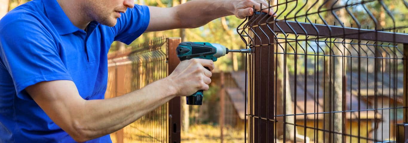 fachowiec przykręca elementy taniego ogrodzenia metalowego
