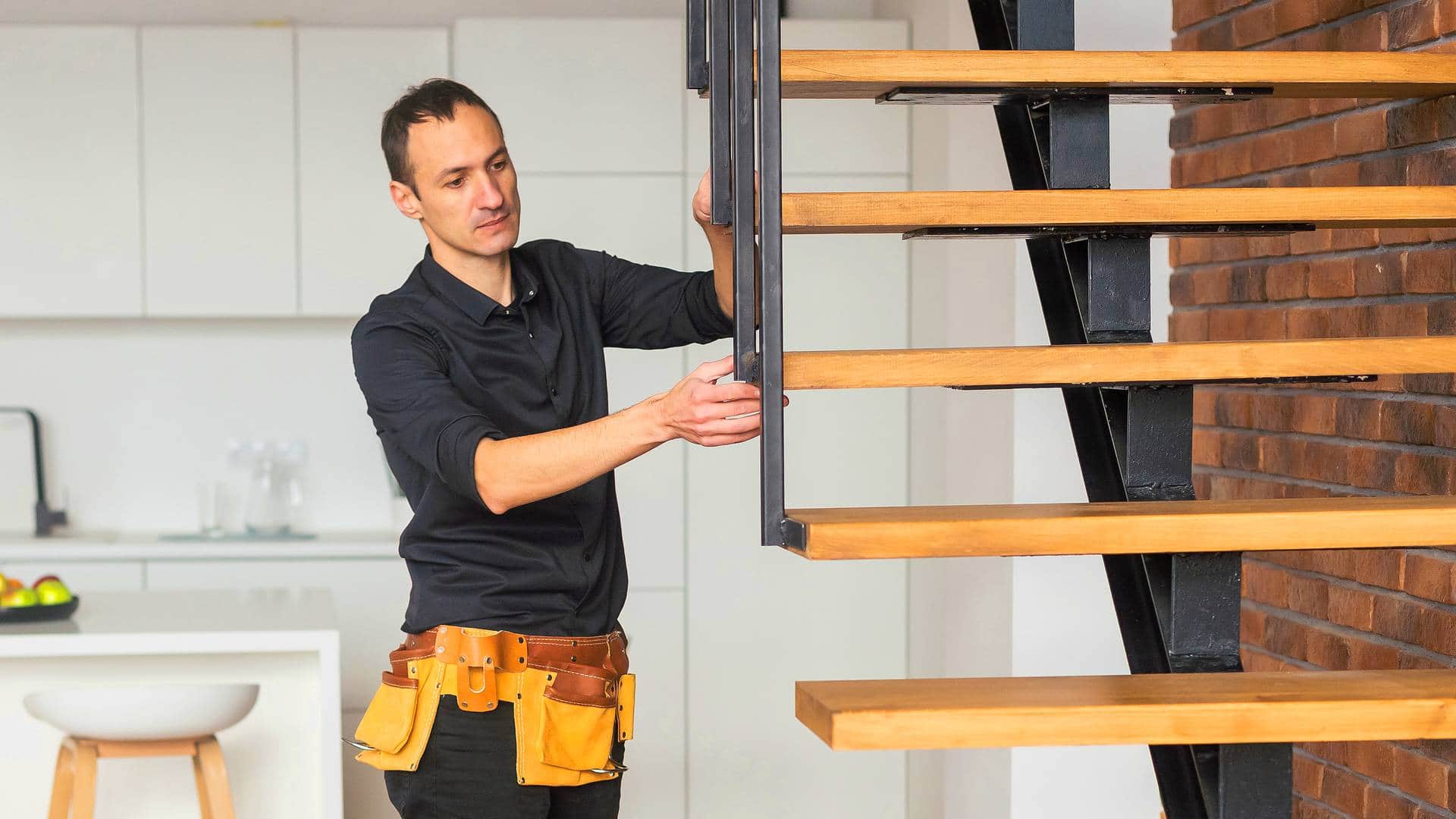 Fachowiec w pasie narzędziowym montujący stopnie nowoczesnych schod&oacute;w drewnianych