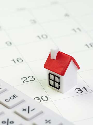 model białego domku z czerwonym dachem i kalkulator leżą na białej kartce kalendarza