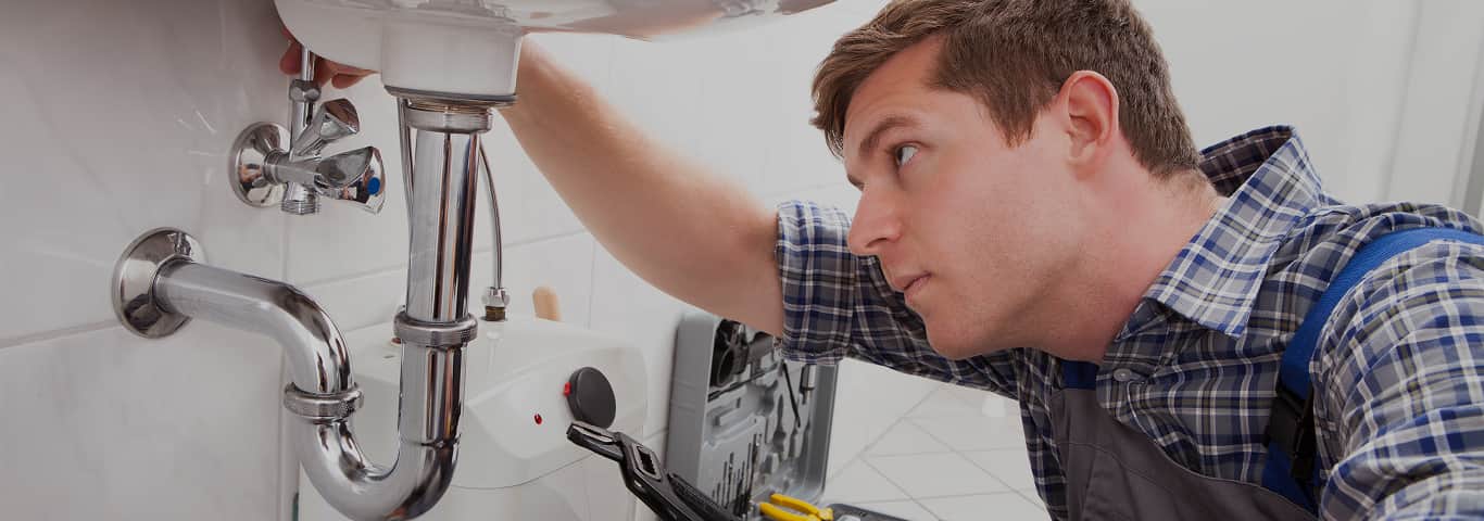 Hydraulik naprawiający instalację wodną pod umywalką w łazience