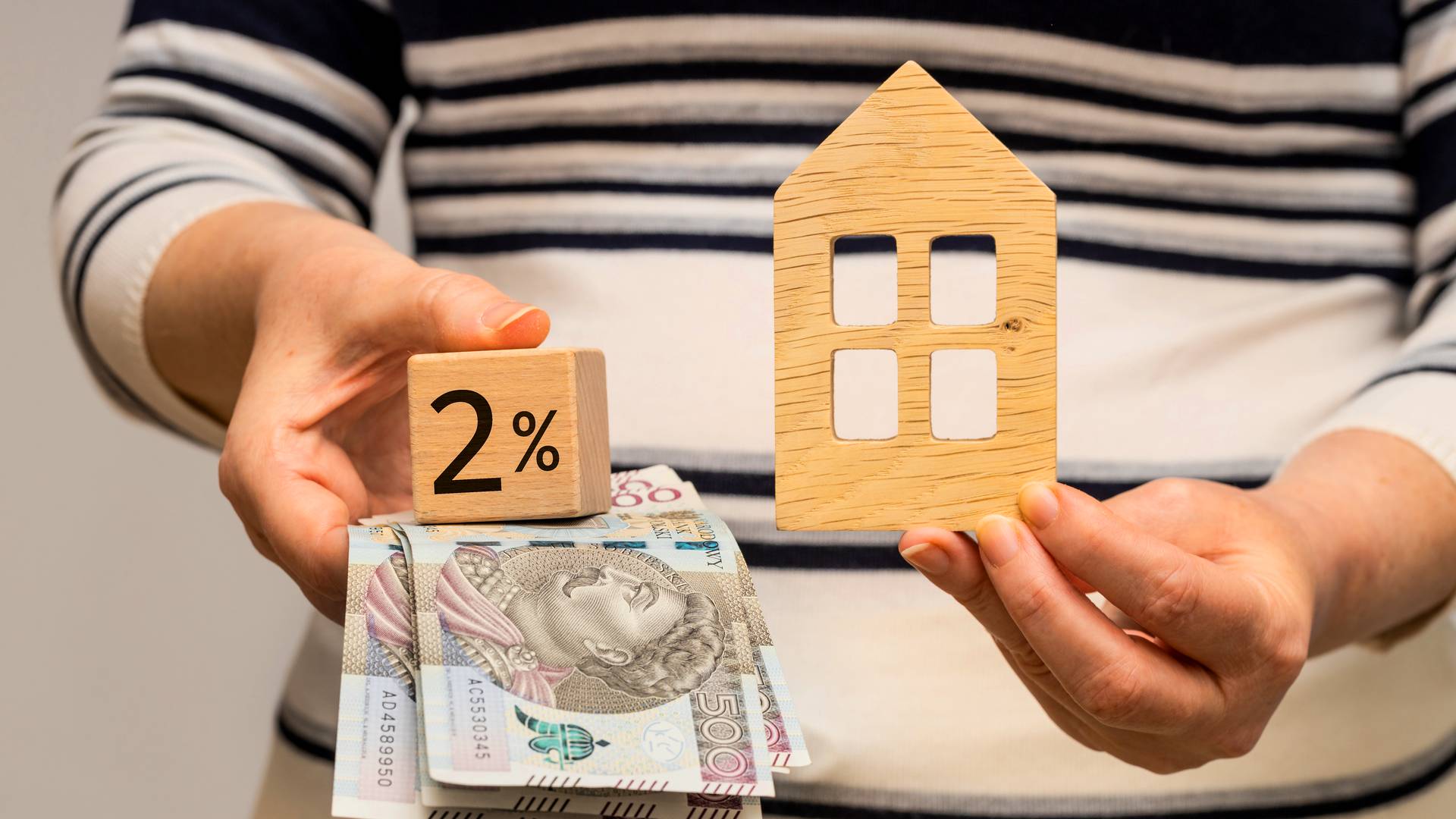 kobieta trzyma w rękach pieniądze z kredytu 2 procent i model domu