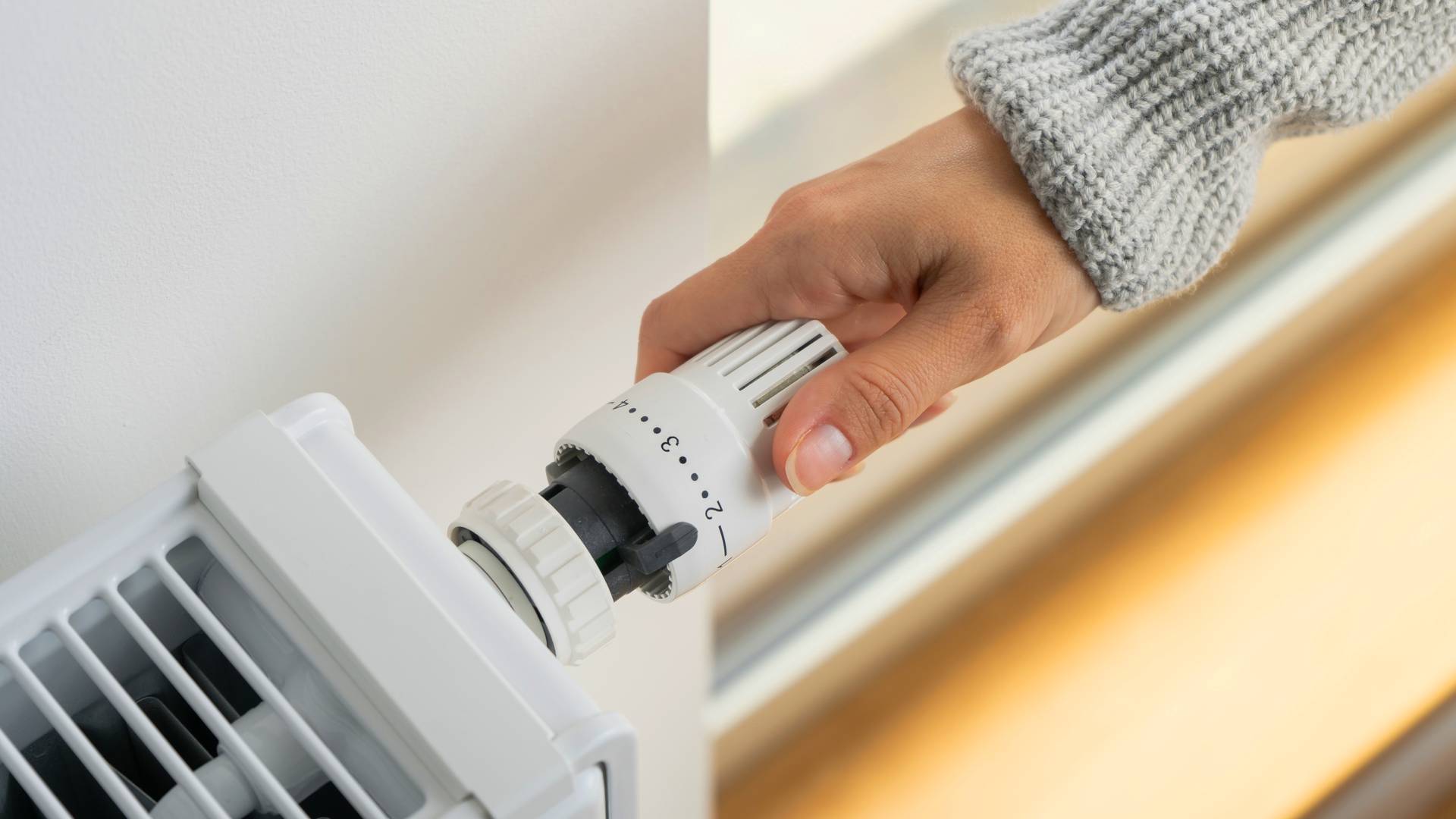 zbliżenie na rękę kobiety ustawiającej termostat grzejnikowy
