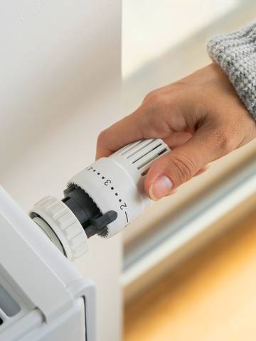 zbliżenie na rękę kobiety ustawiającej termostat grzejnikowy