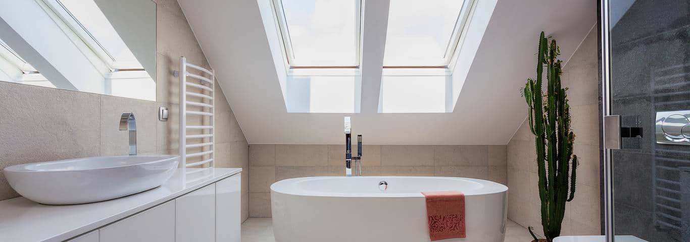Jasna łazienka na poddaszu ze skosami oraz oknami dachowymi i białą wanną wolnostojącą