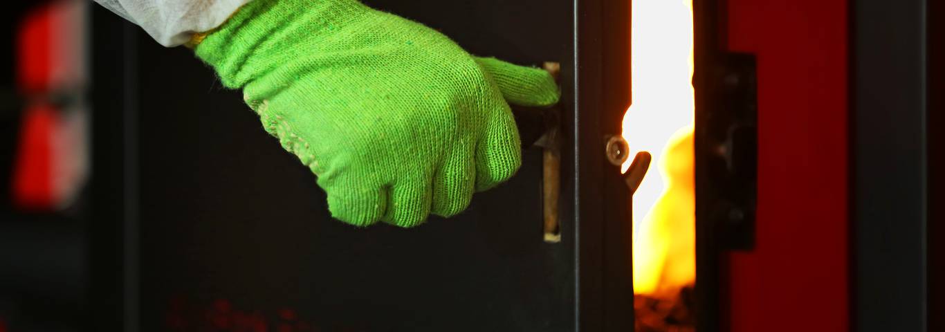 zbliżenie na rękę człoweka otwierającego drzwi kotła na paliwo stałe