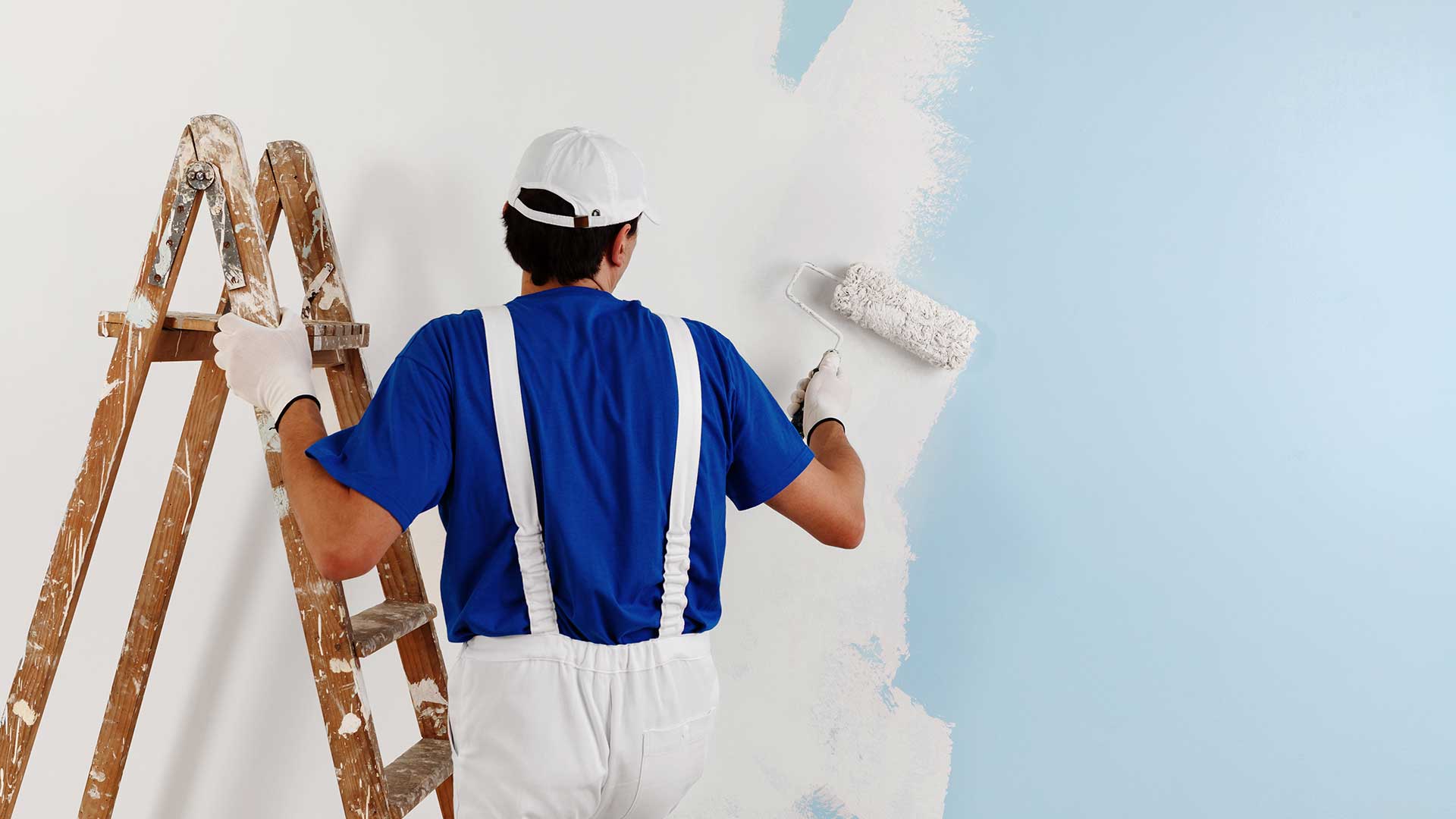 malarz przemalowuje niebieską ścianę na kolor biały -  w 2021
