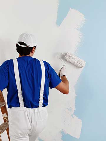 malarz przemalowuje niebieską ścianę na kolor biały