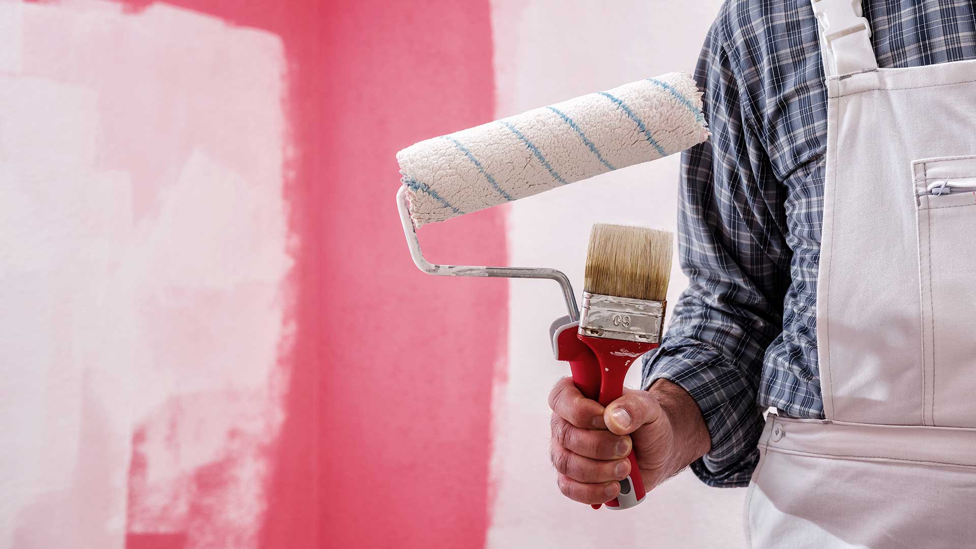 malarz z pędzlem i wałkiem w ręce stoi na tle malowanej ściany -  w 2021