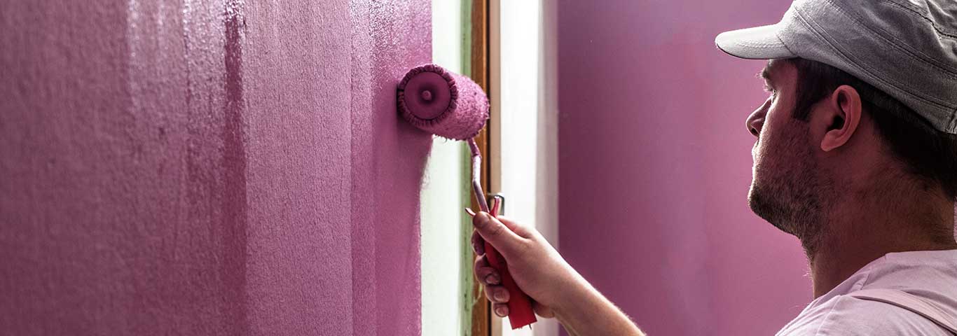 fachowiec maluje wałkiem ściany na kolor różowy