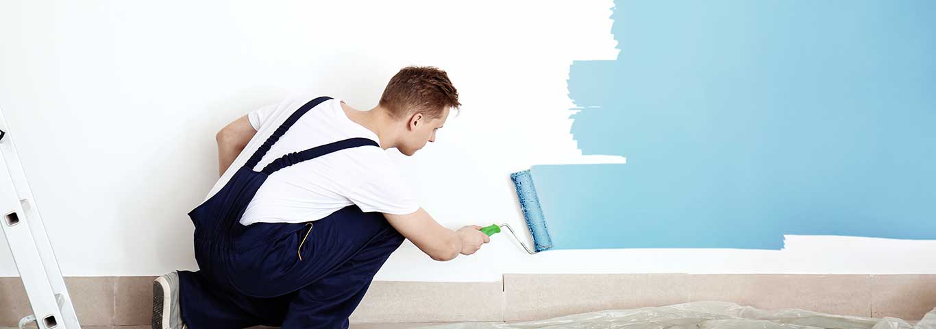 specjalista maluje ścianę wałkiem malarskim na niebieski kolor