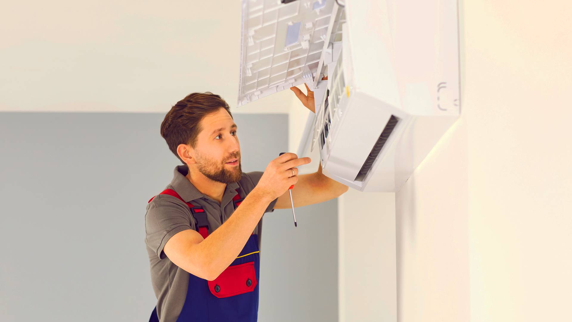 Młody instalator montuje klimatyzację w lokalu usługowym – jaka klimatyzacja będzie najlepsza do sklepu?
