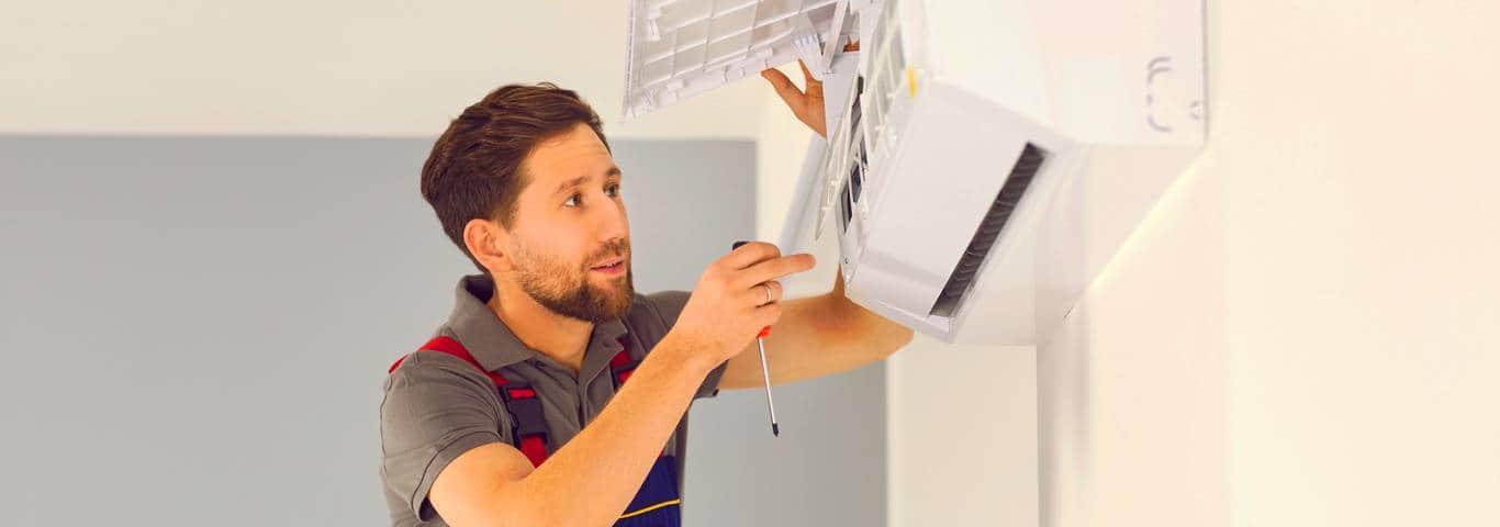 Młody instalator montuje klimatyzację w lokalu usługowym – jaka klimatyzacja będzie najlepsza do sklepu?