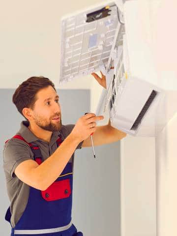 Młody instalator montuje klimatyzację w lokalu usługowym – jaka klimatyzacja będzie najlepsza do sklepu?