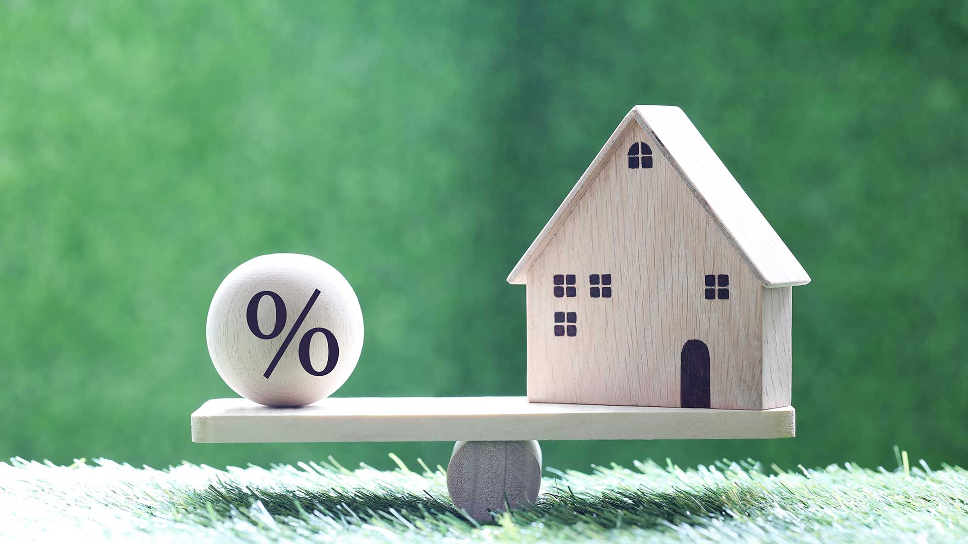 model domu z ikoną symbolu procentu stojący na drewnianej huśtawce na zielonym tle