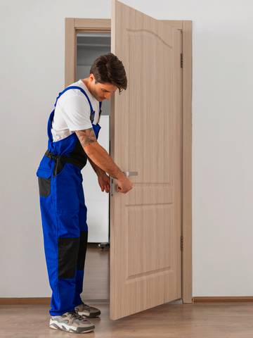 fachowiec w ochronnym ubraniu przykręca klamkę drzwi wewnętrznych