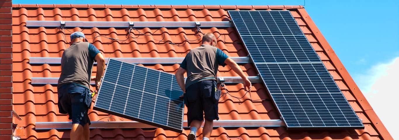 monterzy wnoszą panel fotowoltaiczny na dach domu