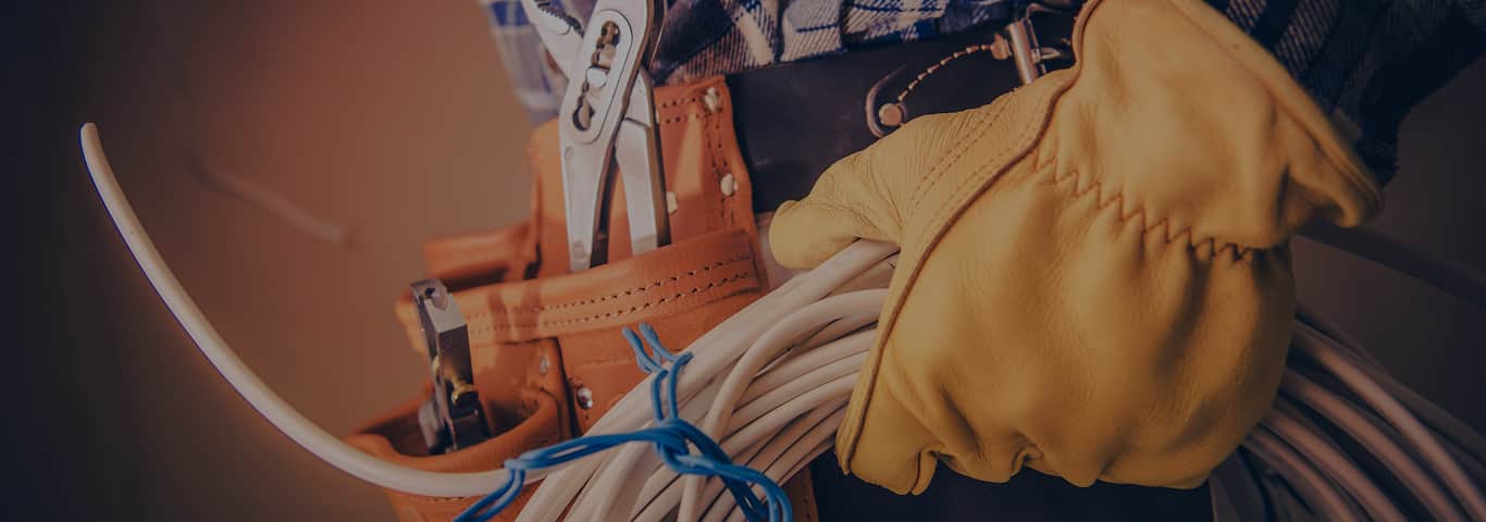 Elektryk w rękawicach ochronnych z przewodami i narzędziami w pasie – gotowy do interwencji przy awarii instalacji
