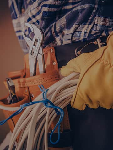 Elektryk w rękawicach ochronnych z przewodami i narzędziami w pasie – gotowy do interwencji przy awarii instalacji