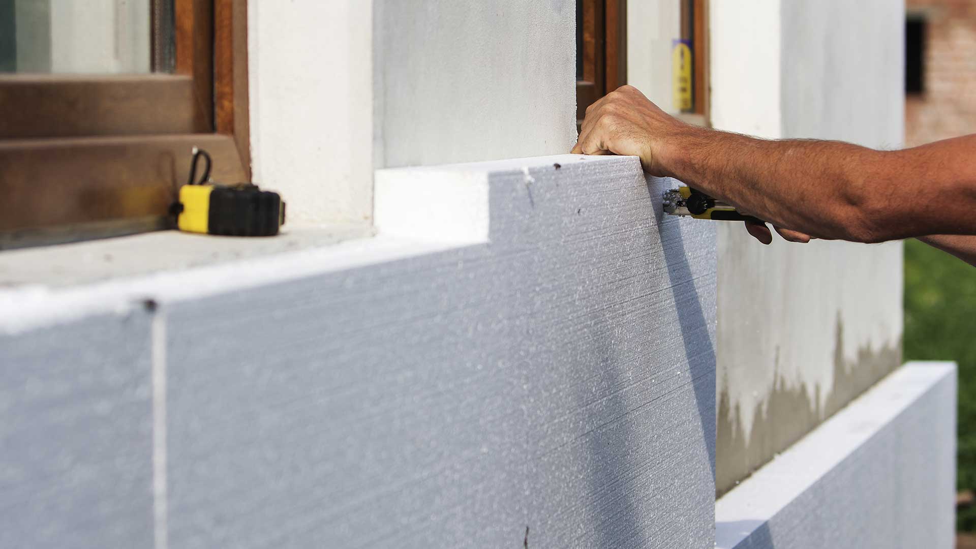 Wykonawca dopasowujący płytę styropianową do elewacji budynku pod oknem