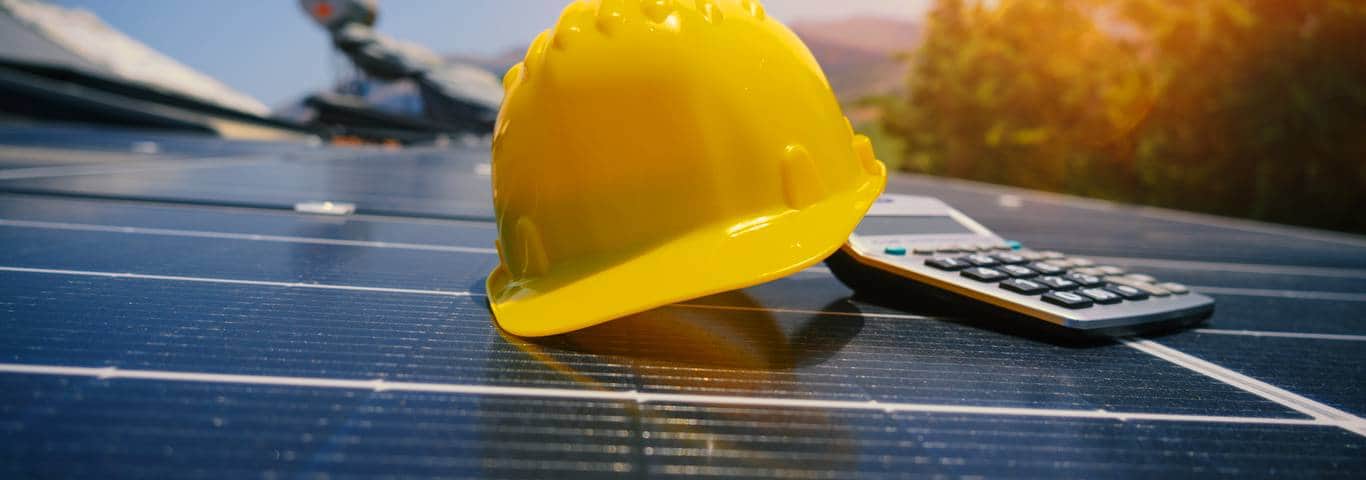 żółty kask i kalkulator na panelu fotowoltaicznym