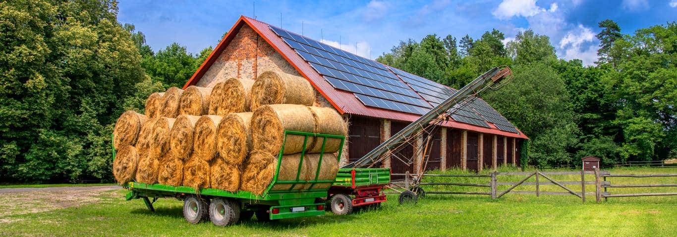 przyczepa z belami siana zaparkowana przed stodola z panelami fotowoltaicznymi na dachu