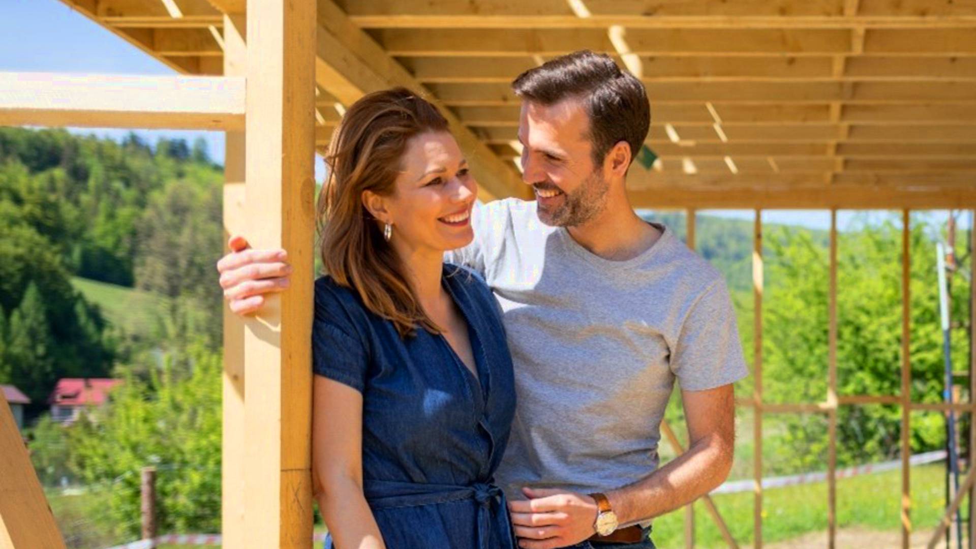 zbliżenie na uśmiechniętą parę stojącą przy szkielecie domu z drewna -  w 2022