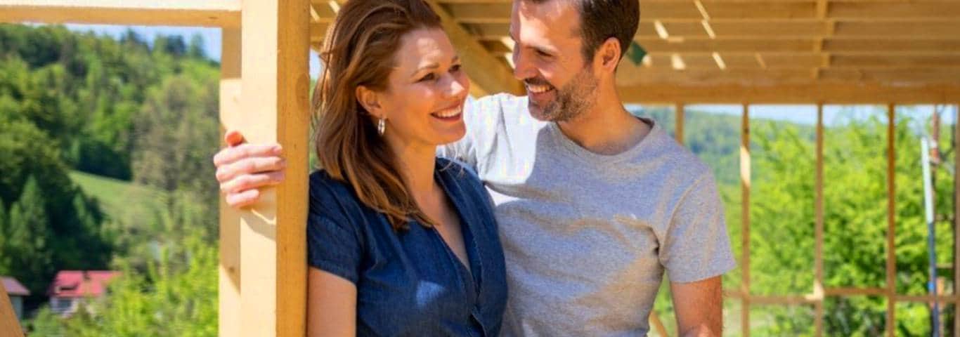 zbliżenie na uśmiechniętą parę stojącą przy szkielecie domu z drewna