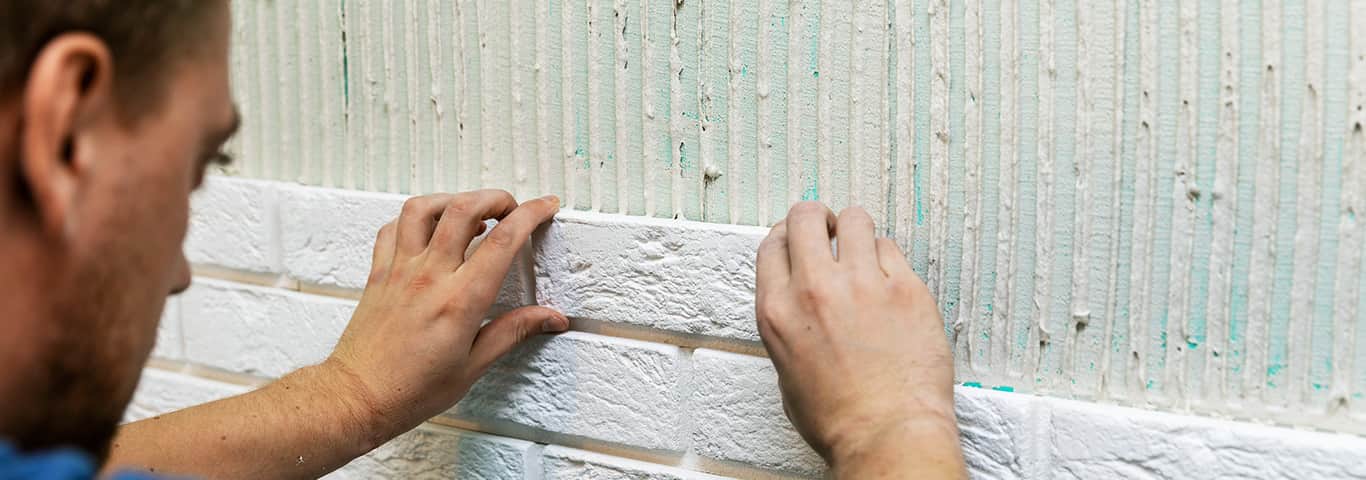 glazurnik układa na ścianie płytki gipsowe imitujące cegłę