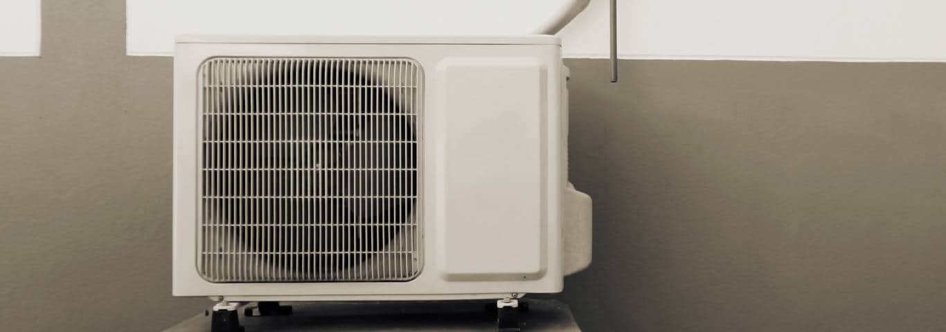 zewnętrzna jednostka pompy ciepła stojąca na fundamencie przy domie jednorodzinnym