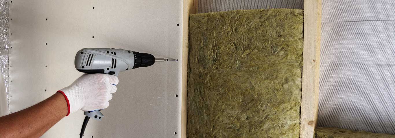 fachowiec mocuje płyty gipsowo-kartonowe za pomocą elektrycznego śrubokręta
