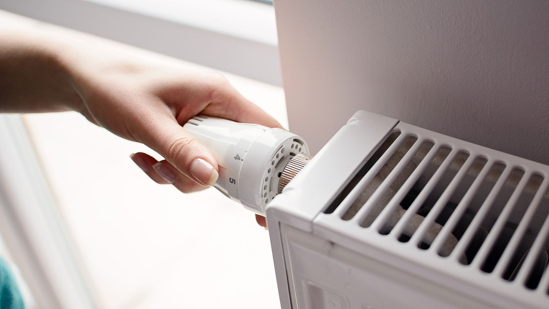 kobieca ręka reguluje zawór termostatyczny w grzejniku do pompy ciepła