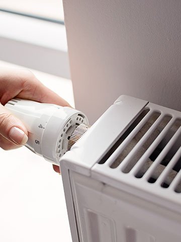 kobieca ręka reguluje zawór termostatyczny w grzejniku do pompy ciepła