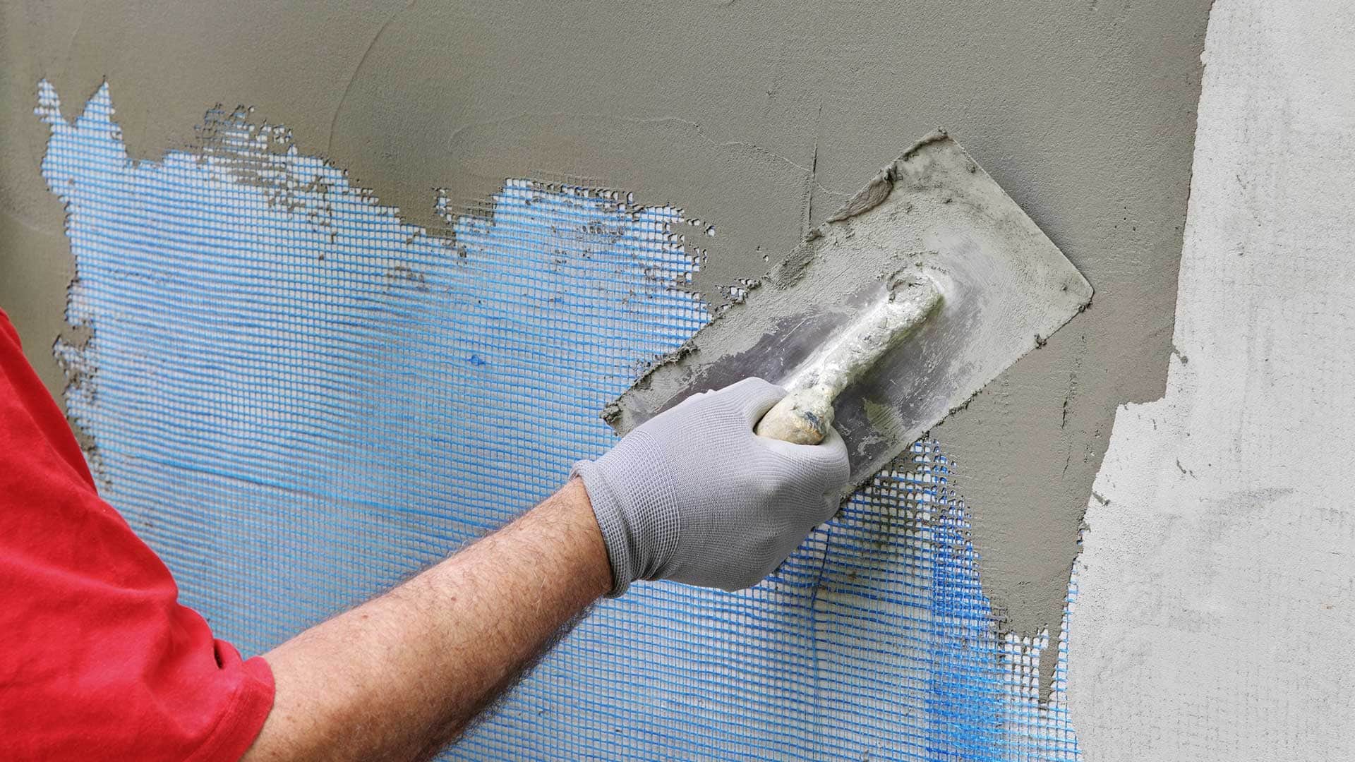 Fachowiec rozprowadza zaprawę klejową na siatce zbrojącej zamontowanej na styropianie – etap przygotowania elewacji pod tynk