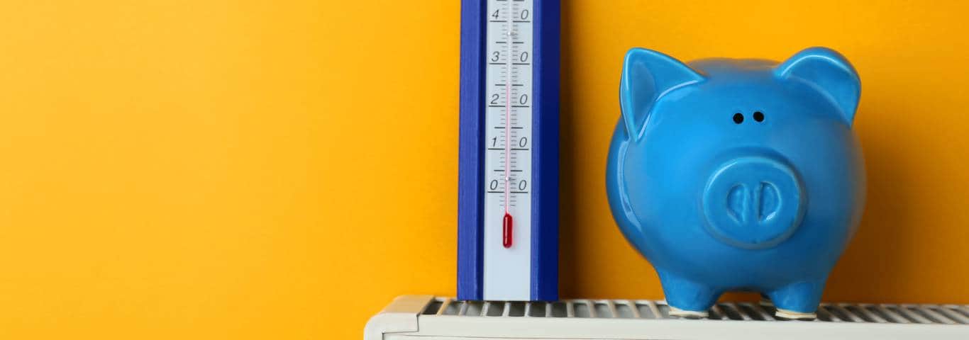 Termometr i niebieska skarbonka ustawione na grzejniku pod ścianą w kolorze żółtym