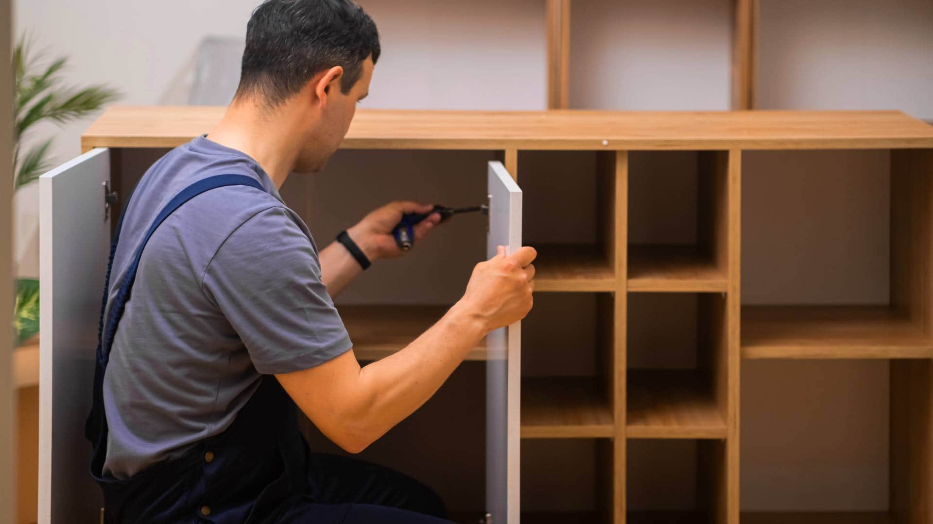 Stolarz w trakcie montażu szafy na wymiar z drewnianymi półkami i białymi frontami