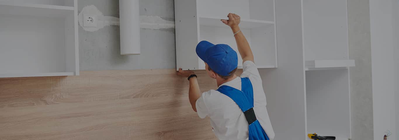 stolarz do mebli na wymiar montuje szafkę kuchenną podczas realizacji zamówienia